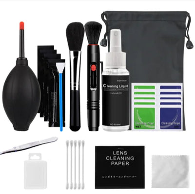 Collection of lens cleaning tools including brushes, spray bottle, wipes, and paper on a white background.